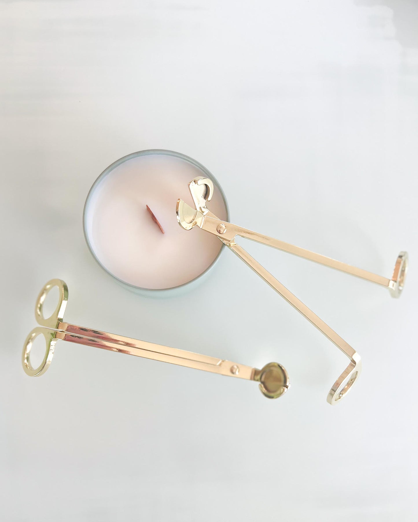 Shiny gold wick trimmers, sitting on top of a Candle Box candle